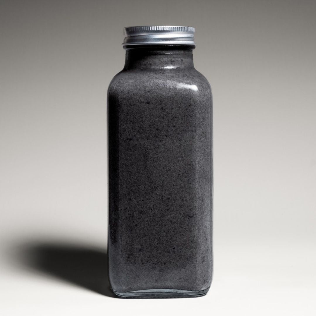 Black coconut charcoal smoothie served in a reusable to-go bottle, placed on a concrete surface with a tropical backdrop.