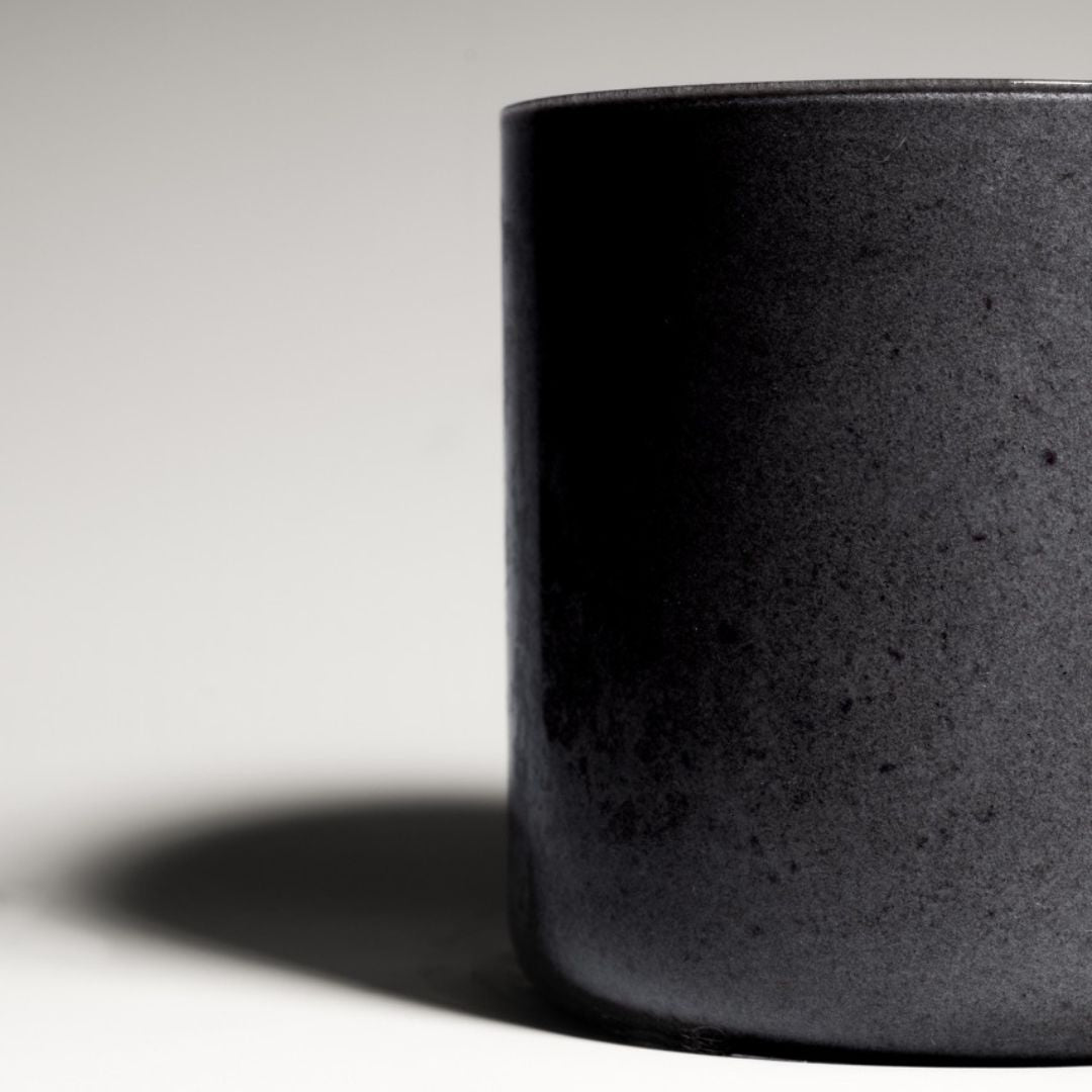 Black coconut charcoal smoothie served in a reusable to-go bottle, placed on a concrete surface with a tropical backdrop.