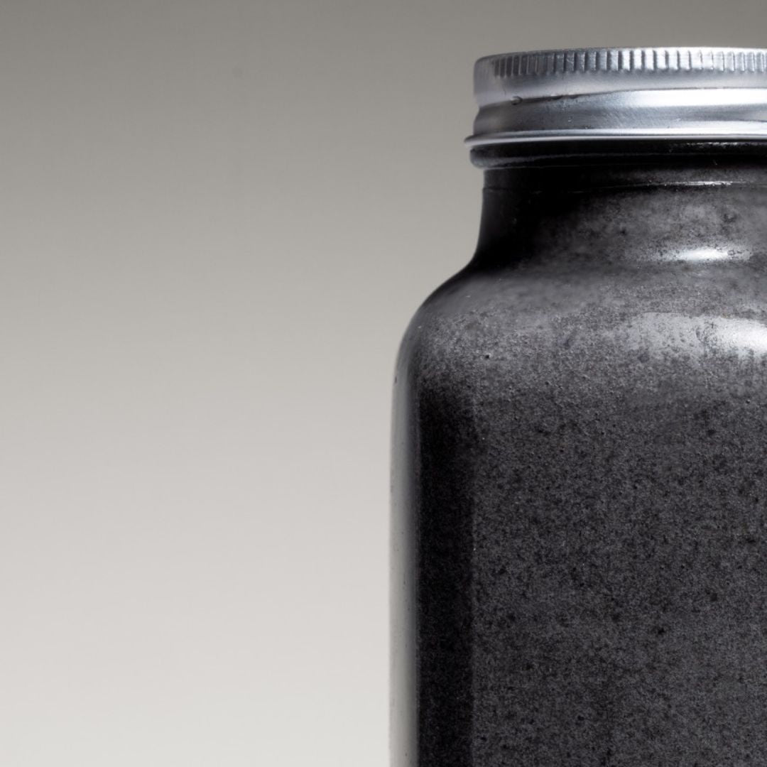 Black coconut charcoal smoothie served in a reusable to-go bottle, placed on a concrete surface with a tropical backdrop.