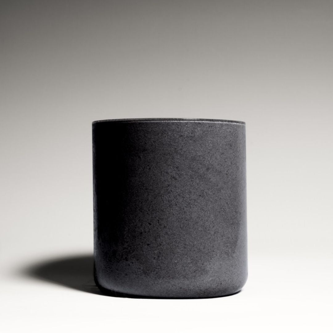 Black coconut charcoal smoothie served in a reusable to-go bottle, placed on a concrete surface with a tropical backdrop.