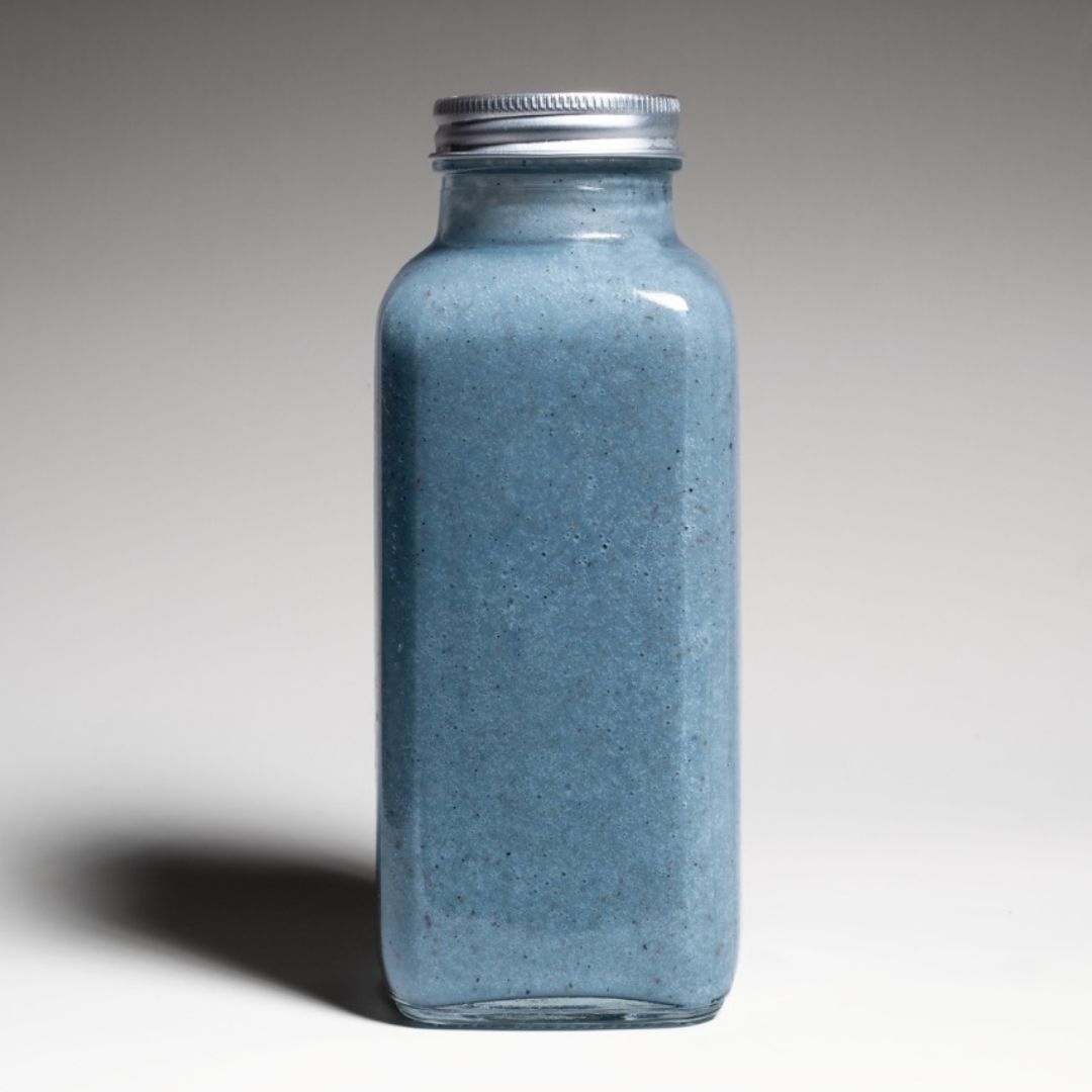 Shot of a bright blue spirulina smoothie in a reusable to-go bottle, captured in a studio with a minimalistic, modern background.