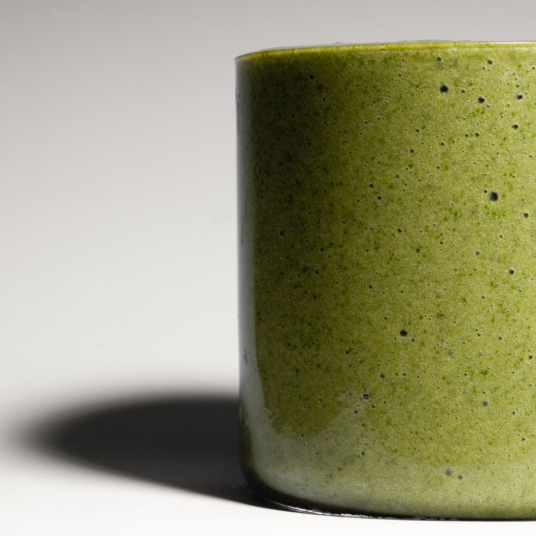 Close-up of a vibrant green Nature’s Balance smoothie in a sleek, minimalistic glass, set in a clean studio setting with soft lighting.